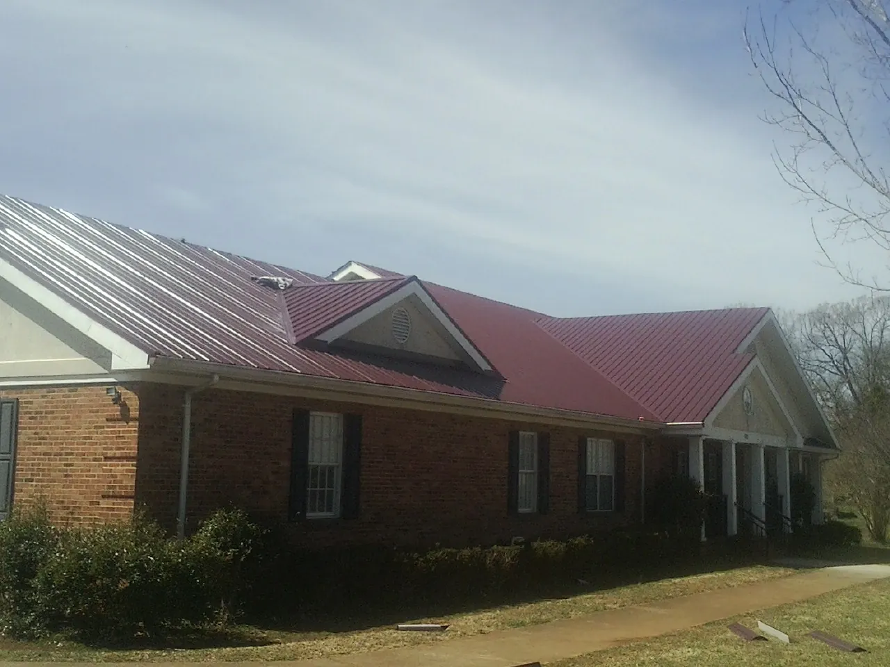 Red metal roof with gabled entries on a long brick building, from a Hail Damage Roof Repair job in Struthers