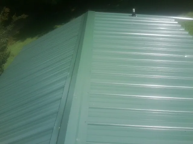 New green metal panels meeting at the ridge of a roof — Flat Roof Repair work by our crew in Struthers