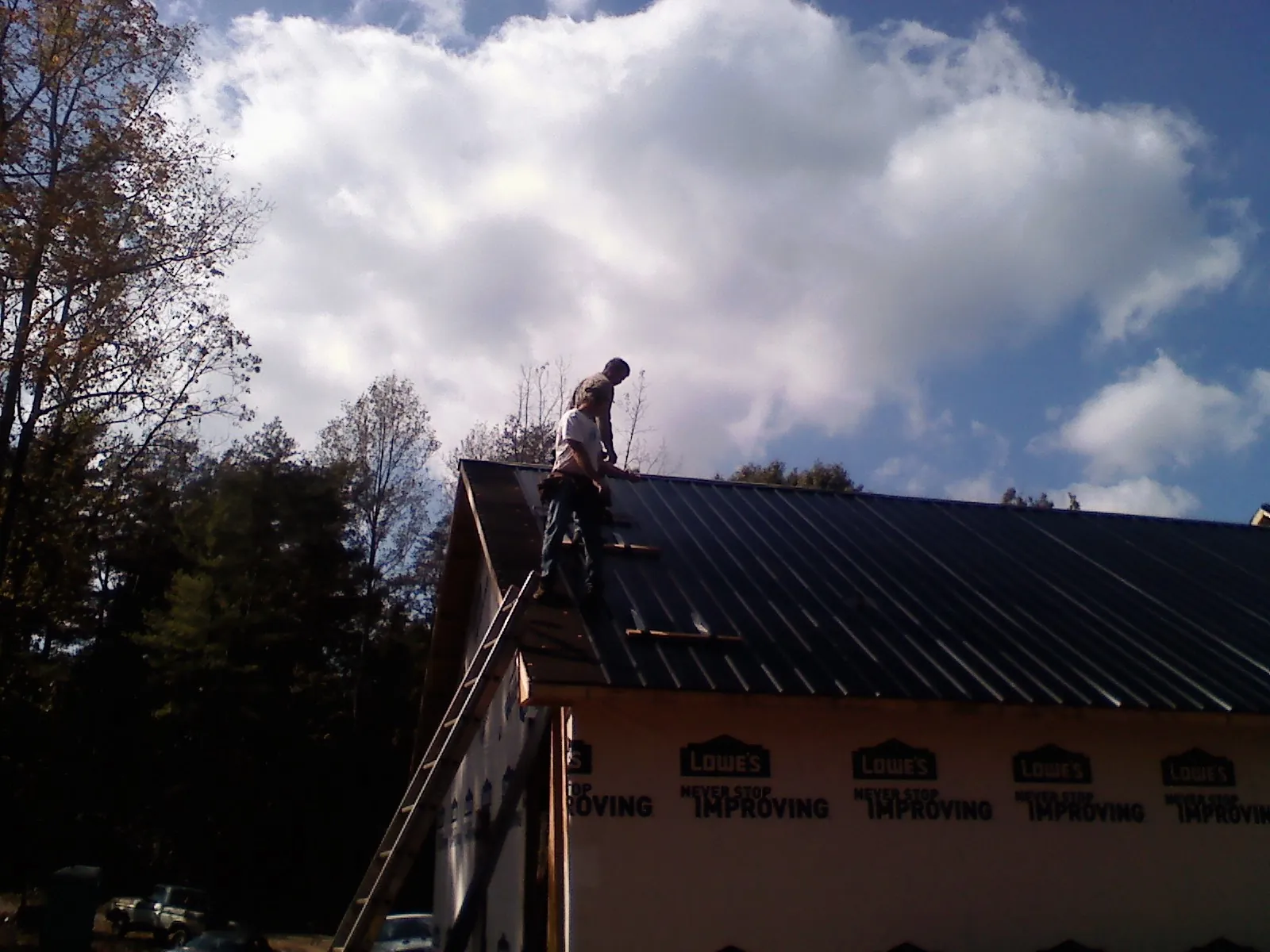 Roofer fastening dark metal panels high against a cloudy sky, from a Roof Inspection job in Struthers